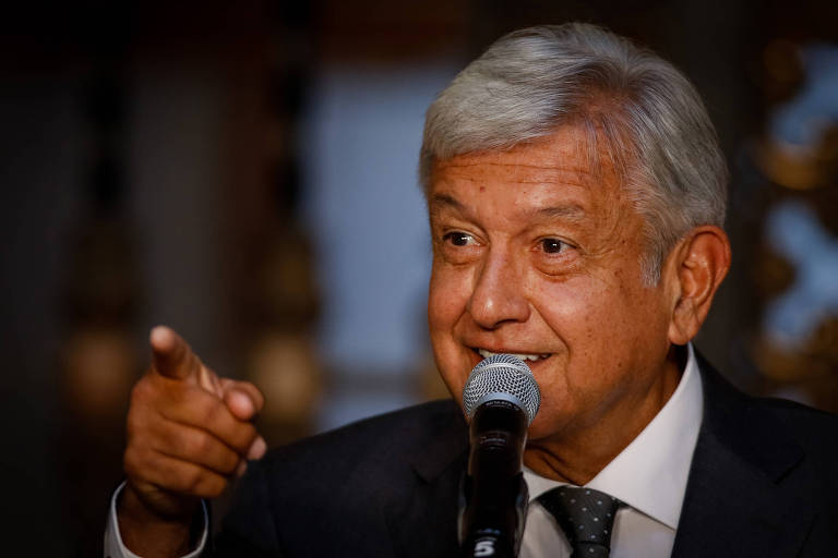 De terno preto, camisa branca e gravata cinza, López Obrador sorri enquanto fala ao microfone e aponta o dedo indicador esquerdo para uma pessoa que não está na imagem. Ele aparece do peito para cima.