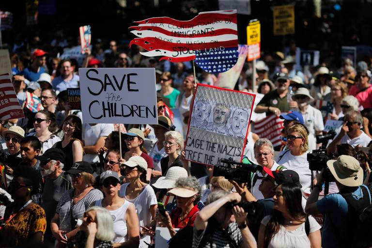 Grupo de cem manifestantes carrega cartazes. Os dois à frente trazem as mensagens "Salvem as crianças" e "Prendam os nazistas. Libertem as crianças", com desenhos de Trump e do secretário de Justiça, Jeff Sessions.