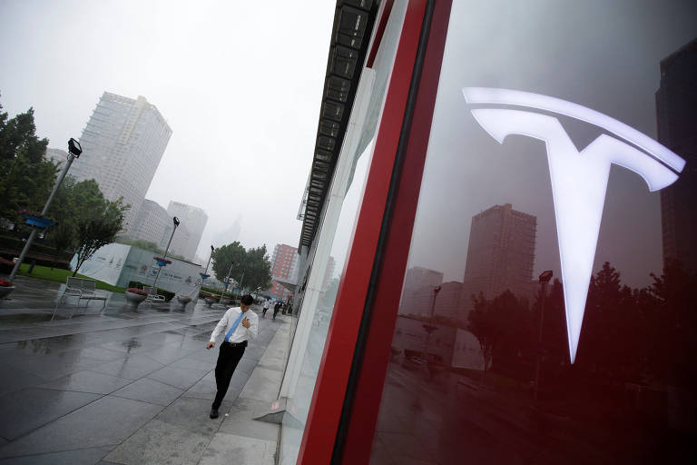 Homem caminha perto de logo da Tesla em Pequim