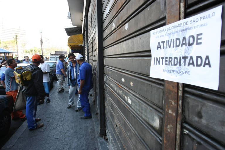 Fachada de estabelecimento comercial interditado após fiscalização na praça da Sé, em São Paulo, com uma placa com os dizeres "Atividade Interditada" colada à porta