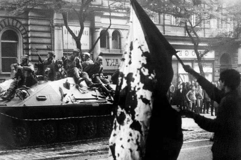 Residente de Praga segura bandeira da Tchecoslováquia manchada de sangue, em frente a um tanque soviético em rua da capital tcheca