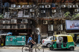 A man cycles past a facade with rows of air conditioners on a hot summer afternoon in New Delhi.