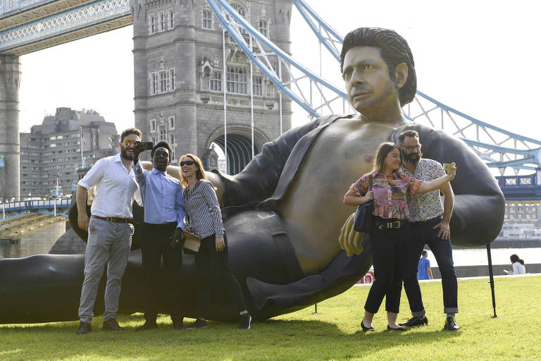 Pessoas tiram foto com uma estátua gigante do ator Jeff Goldblum em uma pose do primeiro "Jurassic Park" (Doug Peters/AP) 
