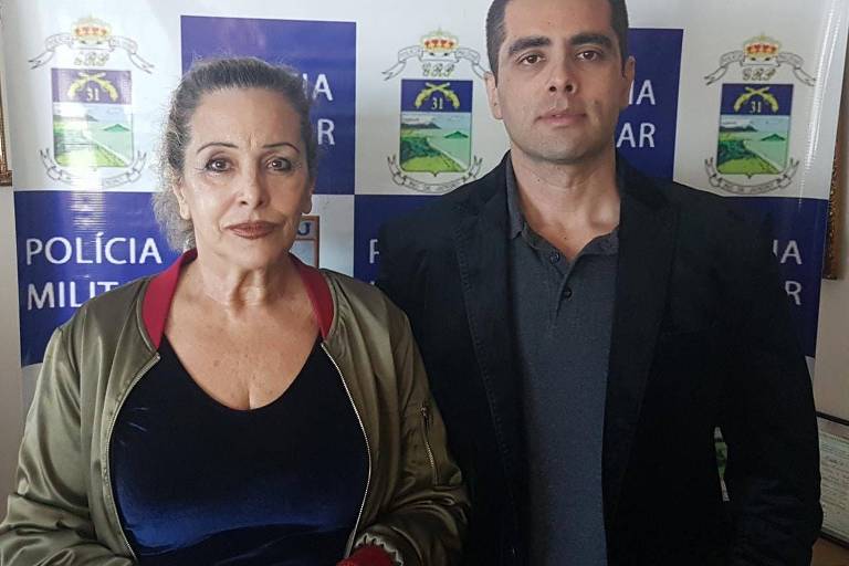 Doutor Bumbum e sua mãe, lado a lado, em foto com nome da PM atrás