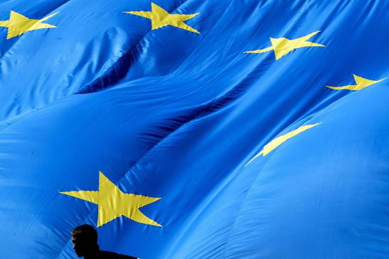 Pessoa caminha em frente à bandeira da União Europeia 