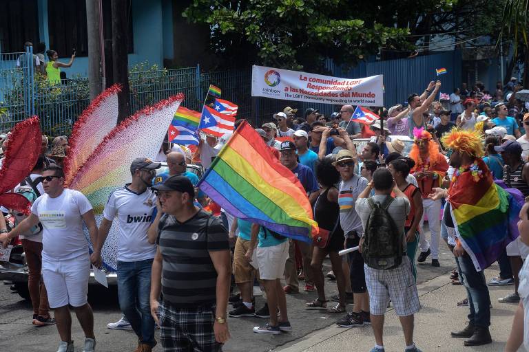 Pessoas desfilam em rua de Havana, em Cuba, com perucas, fantasias e a bandeira do arco-íris