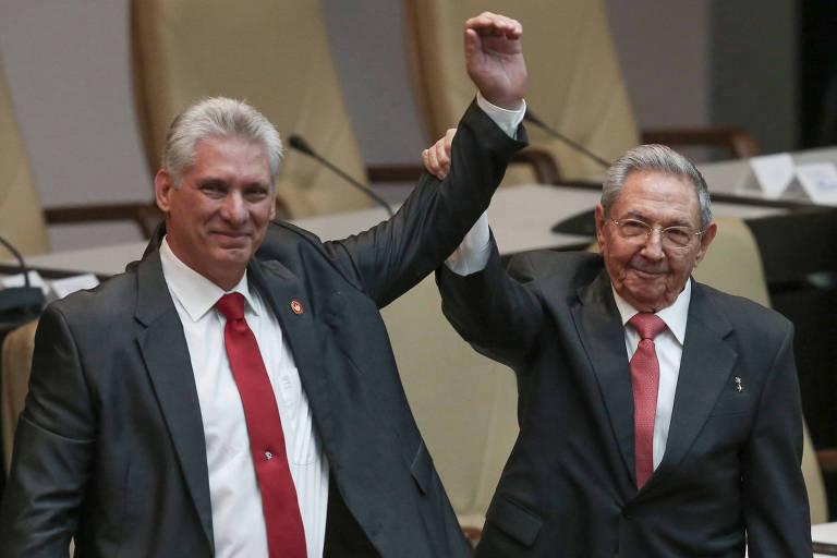 Raúl Castro e Miguel Díaz-Canel unem as mãos no alto. Os dois usam ternos cinza escuro, camisas brancas e gravatas vermelhas