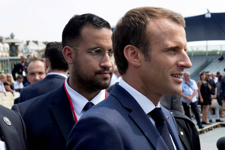 Macron aparece à frente à direita, enquanto Benalla está atrás à esquerda. Os dois usam terno e são vistos da altura do ombro para cima.