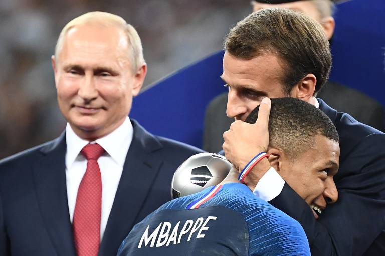 Observado pelo presidente da Rússia, Vladimir Putin, Macron abraça o jogador Kylian Mbappé, enquanto entrega a ele o prêmio de revelação na Copa do Mundo