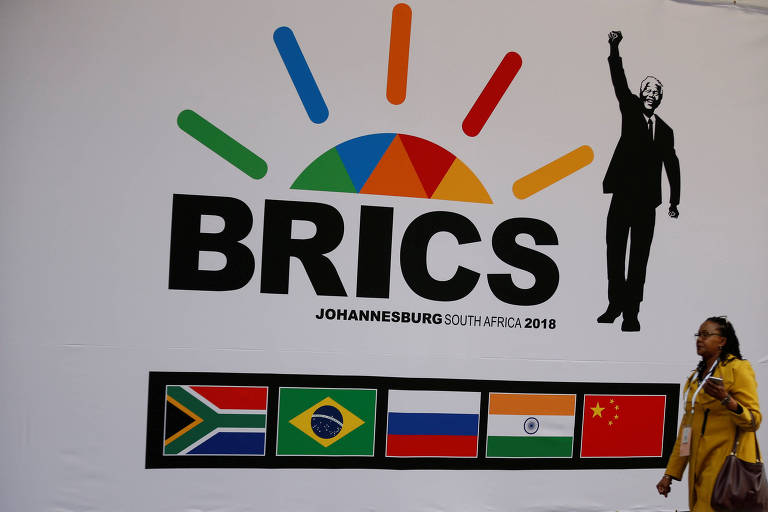 Mulher de vestido amarelo passa antes do quadrado onde estão as bandeiras, na seguinte ordem da esquerda para a direita: África do Sul, Brasil, Rússia, Índia e China. Acima há o logo da cúpula e à esquerda, uma foto de Nelson Mandela acenando.