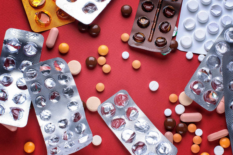 Pílulas e cartelas de pílulas jogadas sobre mesa vermelha