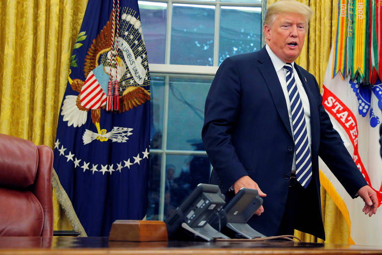 Trump aparece por trás da mesa, que aparece na parte de cima, com dois telefones e parte de sua poltrona, vermelha. A janela é coberta pela metade com cortinas amarelas e, em cada ponta há bandeiras da Presidência dos EUA.