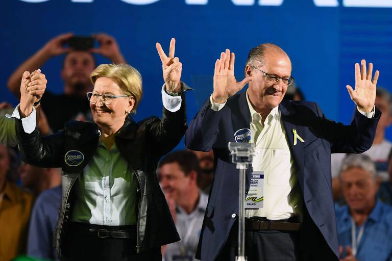 Alckmin aparece levantando as duas mãos e Ana Amélia, fazendo um "V" com a direita. Os dois estão em um palco.