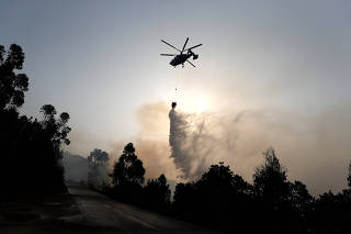 A helicopter drops water on a fire near small village of Monchique