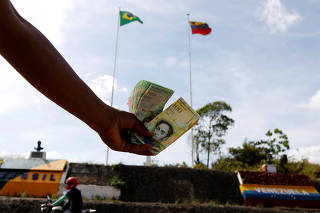 A Venezuelan man displays Venezuelan money at the border with Venezuela, seen from the Brazilian city of Pacaraima
