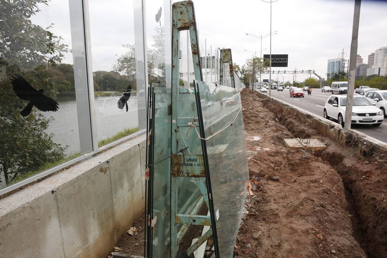 Sete placas de vidro reservas sofrem danos ao ar livre, sob chuva e sol, e podem ser furtadas por quem passa pela marginal (cada uma é avaliada em R$ 4.000); ao fundo, obra de tubulação onde passará cabeamento de câmeras de segurança