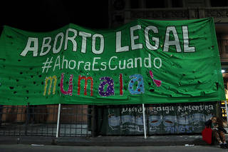A woman sits next to a banner in favour of legalising abortion outside the Congress in Buenos Aires