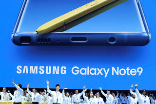 Samsung employees wave from stage beneath an image of the new Samsung Galaxy Note 9 during a product launch event in Brooklyn