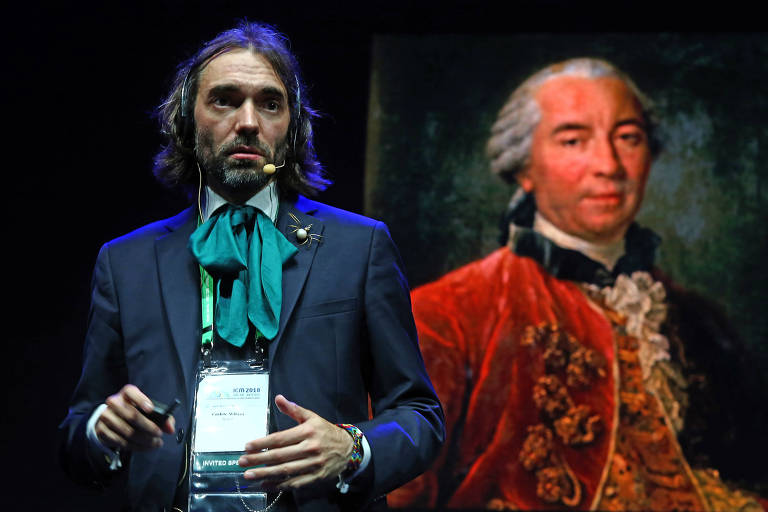 O matemático Cédric Villani, durante palestra no ICM-2018, com roupas vistosas que lembram vestimentas de séculos passados, com um lenço grande no pescoço