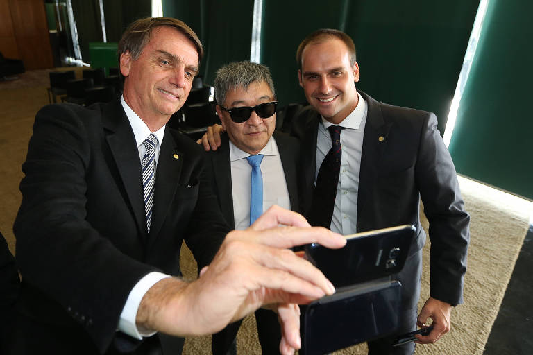 Jair Bolsonaro e Eduardo Bolsonaro tiram foto com o agente Newton Ishii, então chefe do Núcleo de Operações da Polícia Federal de Curitiba (PR), durante visita o plenário da Câmara dos Deputados