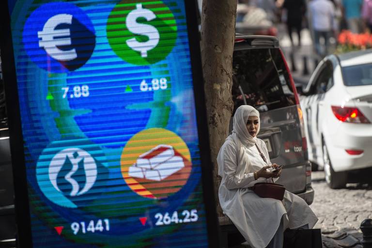 Mulher sentada perto de painel com cotação de moedas na em Istambul, na Turquia