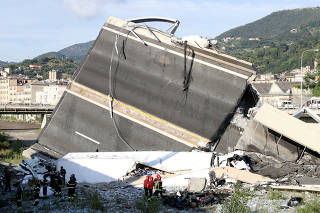 Firefighters and rescue workers stand next to collapsed motorway part at Morandi Bridge site in Genoa