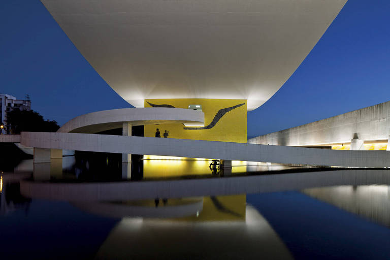 O museu visto por fora, em foto ao anoitecer. A construção tem os traços de Oscar Niemeyer, com as curvas e movimentos característicos do arquiteto