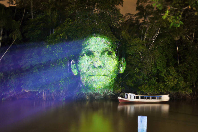 Retrato de mulher projetado em árvores que estão à beira de um rio