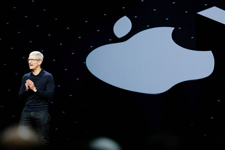 Tim Cook, presidente da Apple, em palco com fundo preto em frente ao logo da Apple