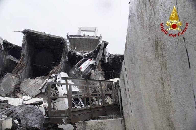 Dois carros capotados são vistos entre os escombros de concreto de uma ponte