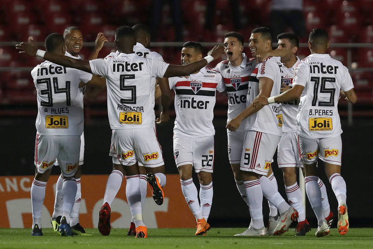 Homem com calção e camisa branca comemoram juntos em gramado