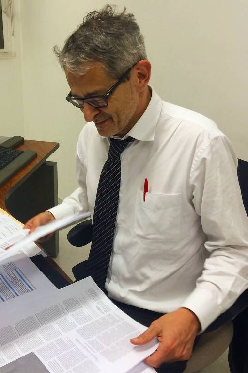 Otavio Frias Filho, sentado em sua mesa e sem terno, examina páginas impressas do jornal para aprovação
