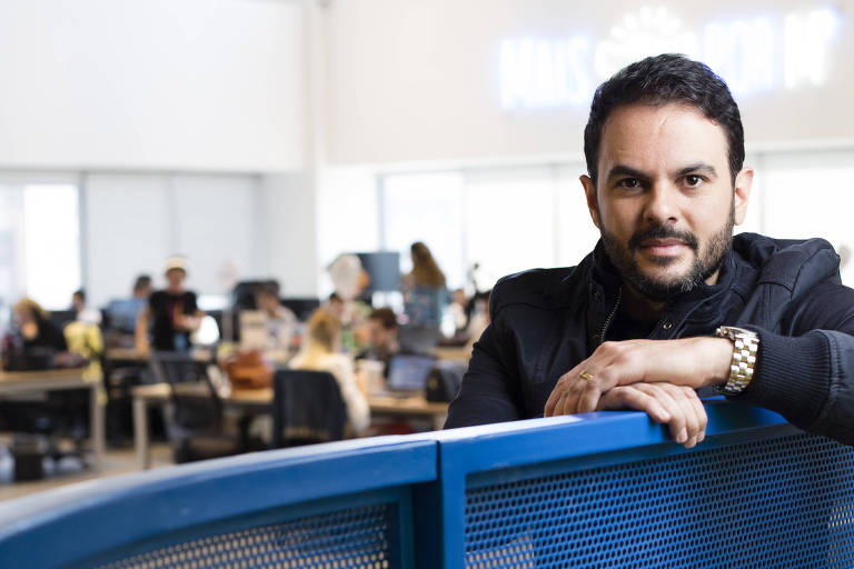 Fábio Rodrigues, sócio da startup Novidá, sentado com as mãos cruzadas sobre encosto de ferro azul