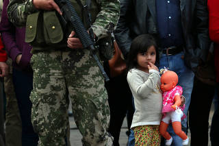 A girl holds a baby doll behind a soldier as she waits for Paraguay's President Abdo Benitez to arrive at a military parade in Asuncion