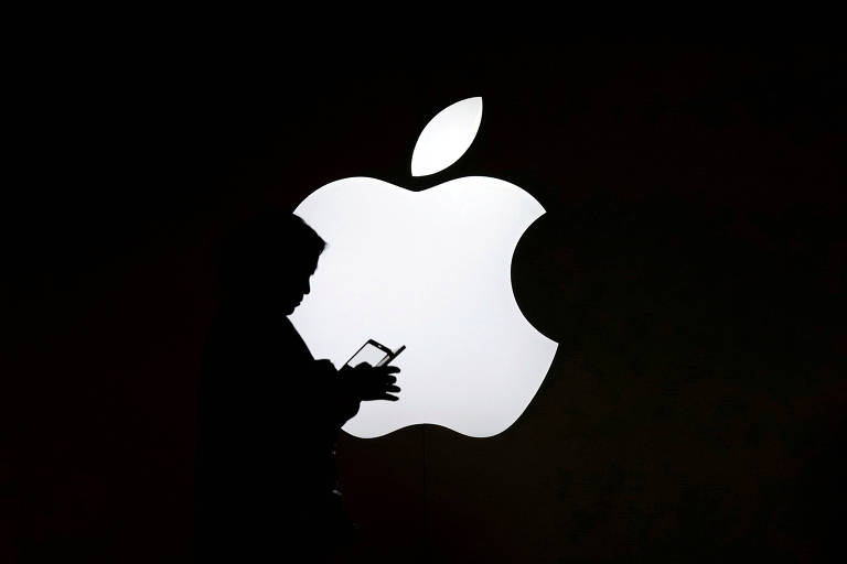 Uma mulher mexe em seu smartphone em frente ao logo da Apple. 