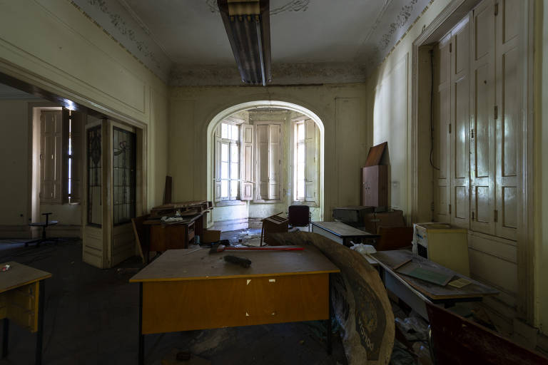 Sala ampla, com passagens em arco, mostra móveis desarrumados deixados pela antiga ocupante da casa, a Polícia Federal