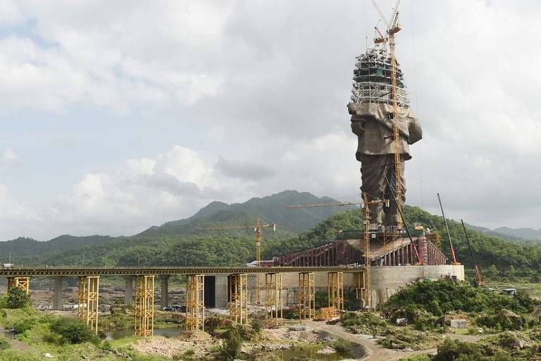 Estátua em construção em uma região com montanhas cobertas por vegetação ao fundo