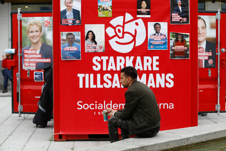 Homem sentado em frente a cartazes do Partido Social-Democratra da Suécia em Estocolmo 