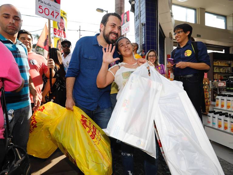 O candidato à Presidência Guilherme Boulos (PSOL) segura as sacolas de uma eleitora para posar para fotos durante caminhada e panfletagem, na rua 13 de maio, na região central de Campinas