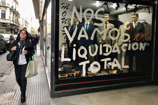 People walk by a store that is going out of business in Buenos Aires