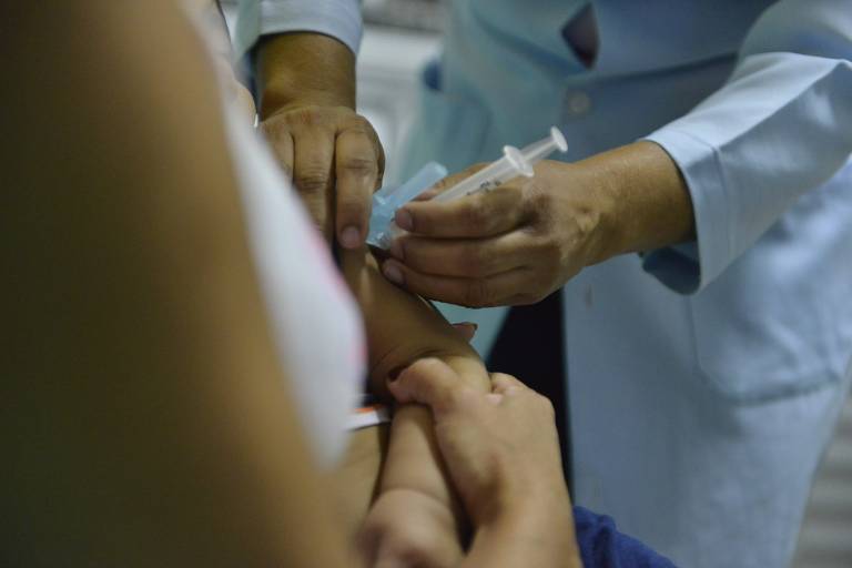 Imagem em close mostra profissional da saúde vacinando criança