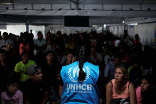 A member of United Nations High Commissioner for Refugees talks with Venezuelans as they queue in line to receive a vaccine after showing their passports or identity cards at the Pacaraima border control