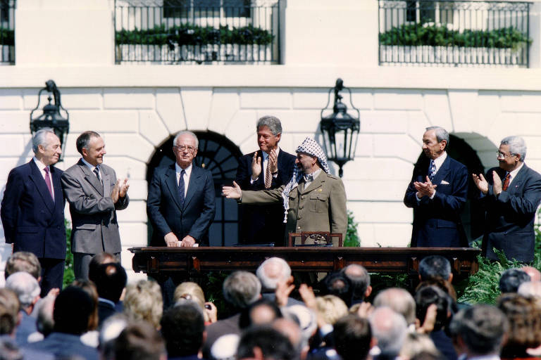 O então líder da Organização pela Libertação da Palestina (OLP), Yasser Arafat, gesticula para o então primeiro-ministro de Israel,  Yitzhak Rabin, enquanto os dois são observados pelo presidente dos EUA, Bill Clinton, na assinatura do acordo de paz entre israelenses e palestinos, em 13 de setembro de 1993. 