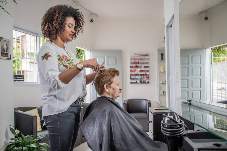 Retrato da empresária e cabelereira Julyana Carvalho dos Santos (29) em seu salão de beleza no Taboão da Serra. Na foto produzida, ela corta o cabelo de sua tia Joana de Carvalho (57), que trabalha de manicure com ela.