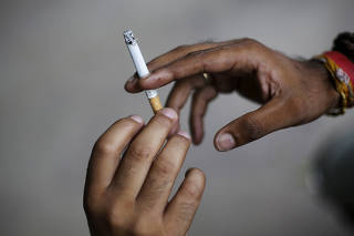FILE PHOTO: A man passes a cigarette to another while smoking in New Delhi
