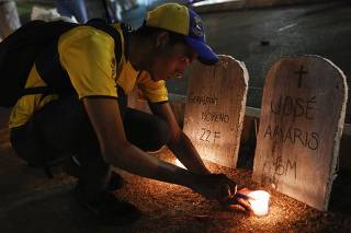 An anti-government protester lights candle in front of mock tombstones with names of victims of violence, during a protest against Nicolas Maduro's government at Altamira square in Caracas