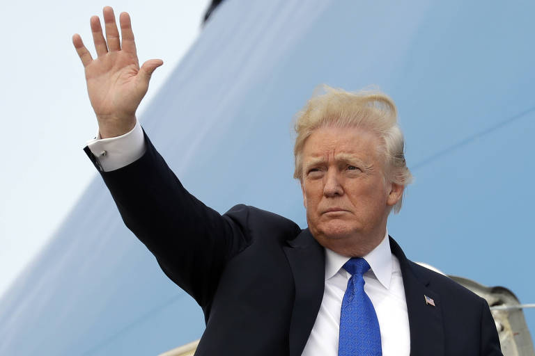 Trump acena com a mão direita da escada do Air Force One. Ele usa um terno preto, camisa branca e uma gravata azul.