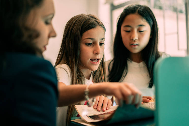 Lívia Leoni Domingues, coordenadora da seção circulante da biblioteca, auxilia Luiza Alarcon, 10, no centro, e Carolina Watanabe, 11, à direita; 
