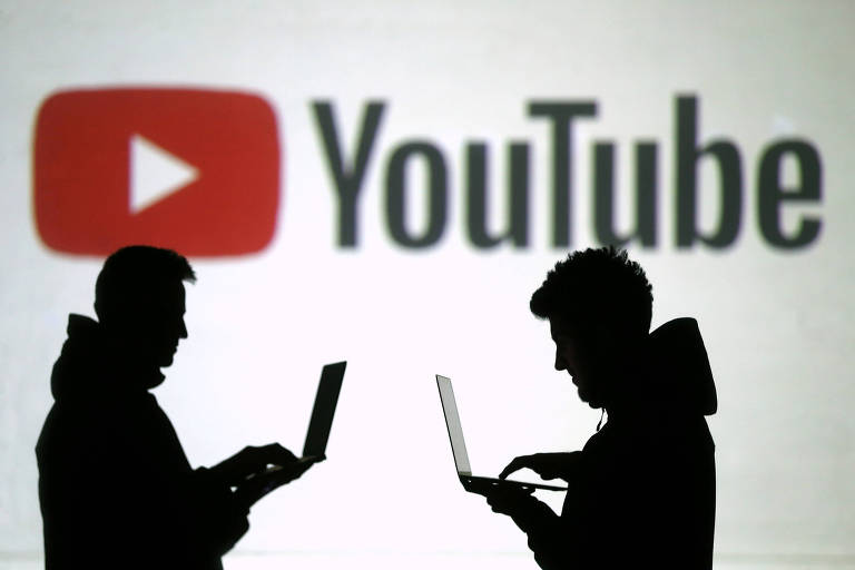 Pessoas em frente ao logo do YouTube; serviço premium do site custa R$ 20,90 no Brasil