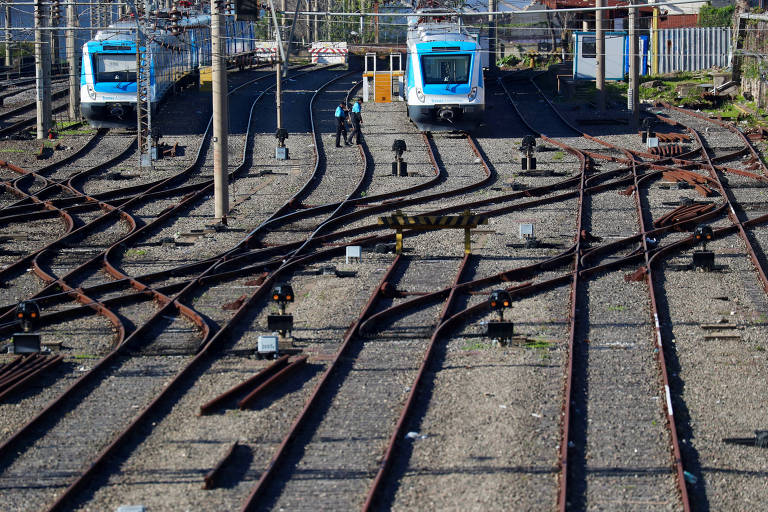 Dois trens são vistos parados ao fundo de uma série de cinco linhas férreas
